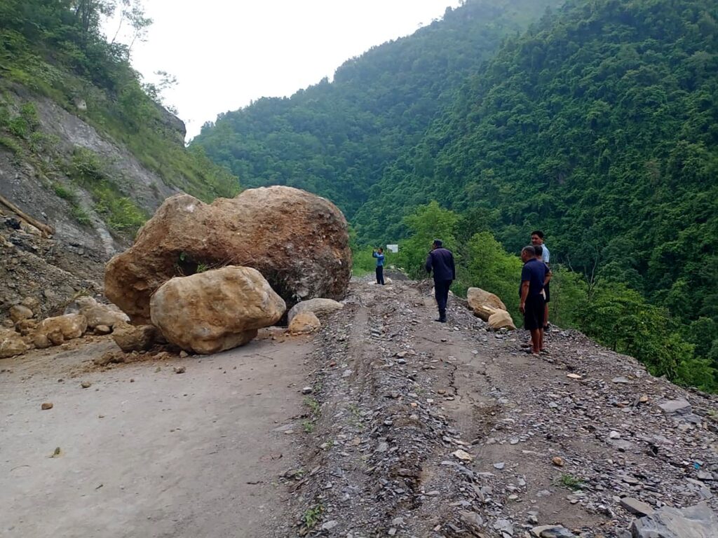 Landslide blocking Kaligandaki Corridor road in Gulmi district caused by heavy rainfall, with rocks and mud covering the roadway and rescue workers nearby.
